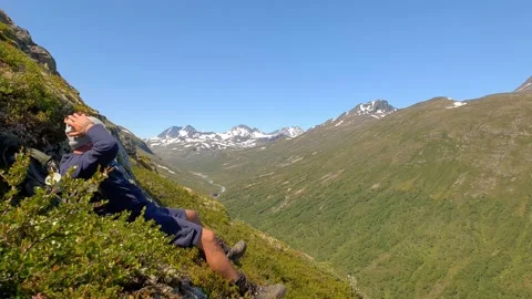 Hiker sits down to rest and enjoys view over mountain range in Norway Stock Footage 156780441