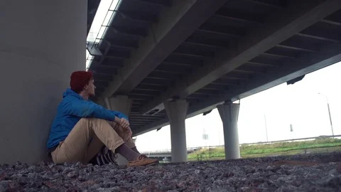 Hiker sitting on tground under road bridge. Car traffic on road at background Stock Footage 80286234