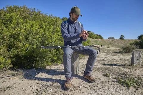Hiker sitting on wooden post using smartphone outdoors Stock-Fotos