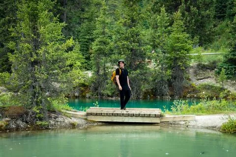 Hiker on small bridge over vibrant blue glacial stream in the forest Stock Photos
