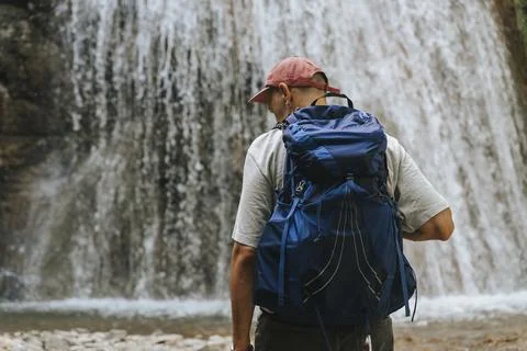 Hiker standing before a waterfall with a backpack. Stock Photos