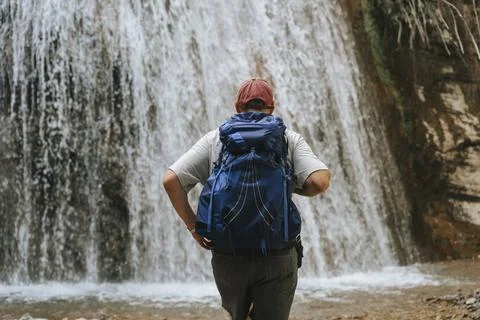 Hiker standing before a waterfall with a backpack. Stock Photos