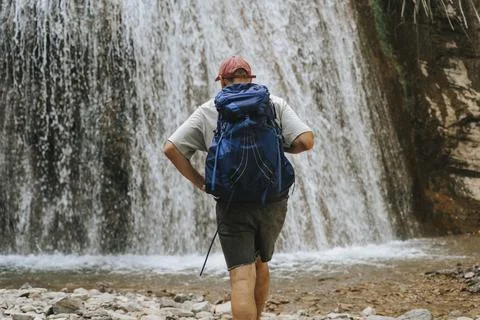 Hiker standing before a waterfall with a backpack. Stock Photos