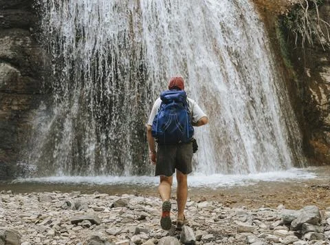 Hiker standing before a waterfall with a backpack. Stock Photos