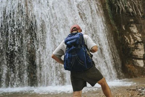 Hiker standing before a waterfall with a backpack. Stock Photos