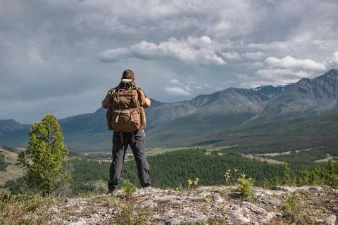 Hiker stands with backpack on background of mountains Stock Photos
