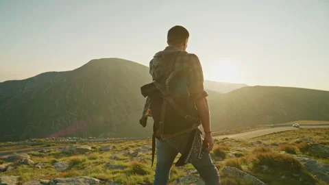 Hiker stands on a mountain looking at the sunset over hills and a road in the Stock Footage 345632269