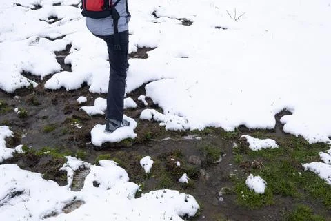A hiker steps on a patch of snow on a muddy stream in a winter landscape Stock Photos