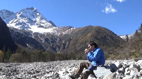 Hiker taking a rest and drinking coffee, snow mountains in the background Stock Footage 43503406