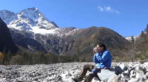 Hiker taking a rest and drinking coffee, snow mountains in the background Stock Footage 43503472