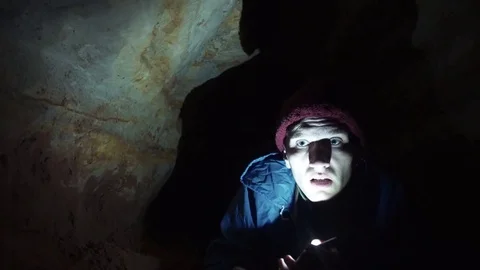 Hiker using smartphone laying on ground into narrow hole in cave with flashlight Stock Footage 80053573