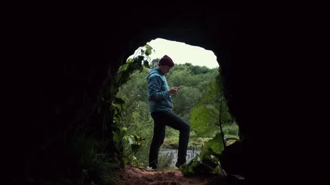 Hiker using smartphone standing near exit from cave. Deep forest at background. Stock Footage 80053845
