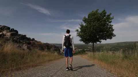 Hiker walking away from camera on a paved trail in the mountains in Portugal Stock Footage 314019916