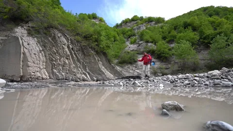 Hiker Walking Between Mountain River and Pond 動画素材 308961330