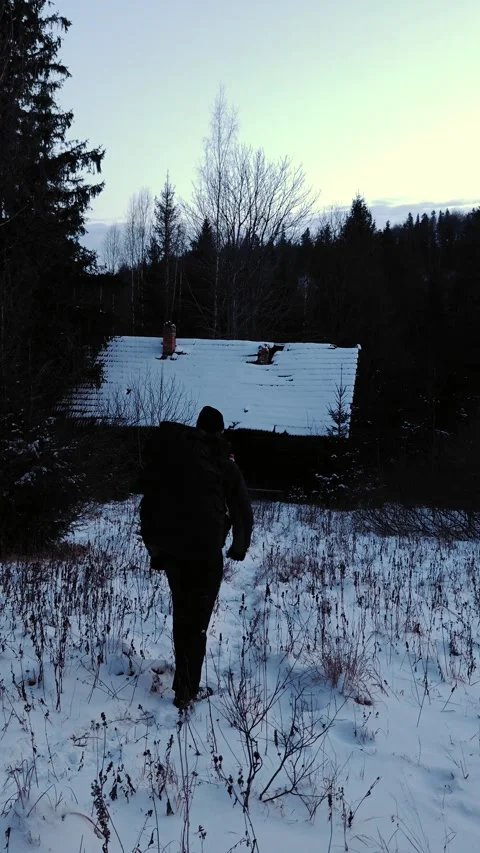 Hiker walking in deep snow towards a remote mountain log cabin Stock Footage 333901780