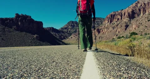 Hiker Walking Down Desert Road with Mountains in Background Vídeo Stock 323805983