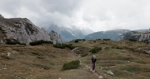 Hiker Walking Mountain Trail Alpine Plateau Dramatic Peaks Background Stock Footage 332446056