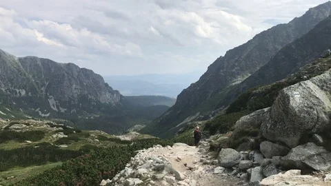 Hiker walks down the trail as we pan off to appreciate the panorama Видео 80490190