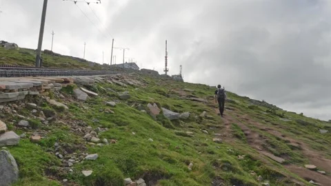 Hiker walks up mountain trail with train tracks and radio mast in France Stock Footage 341459520