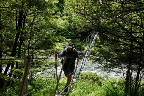 A hiker walks over a wire suspension bridge Stock Photos