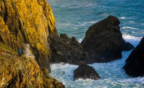 A hiker watches the waves crash on the rocks at Kynance Cove, Cornwall,UK Stock Photos