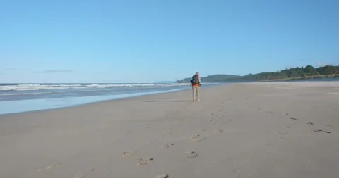 Hiker wearing a red jacket walking alone on a remote beach Stock-Footage 279859196