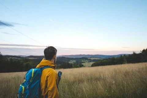 Hiker in a yellow jacket with a blue backpack overlooking a peaceful landscap 스톡 사진