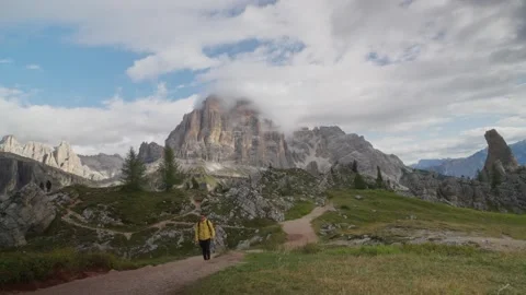 Hiker in yellow jacket walking mountain trail with scenic peaks Dolomites Italy Stock Footage 320179127