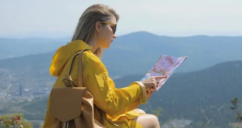 Hiker in a yellow raincoat looking at map from mountain top. woman with map in Stock Footage 94358711