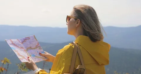 Hiker in a yellow raincoat looking at map from mountain top. woman with map in Video stock 94358725