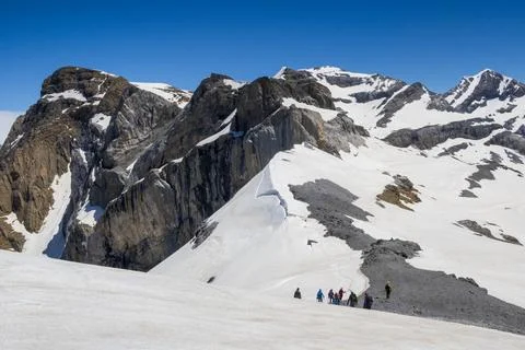 Hikers Below Dramatic Limestone Peaks and Summer Snow in the Pyrenees 스톡 사진
