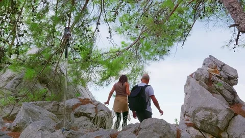 Hikers exploring rocky mountain terrain beneath shade trees 库存影片 337497898