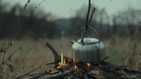 Hikers make a campfire on the grass during a hike and boil water in an iron Stock Footage 206159479