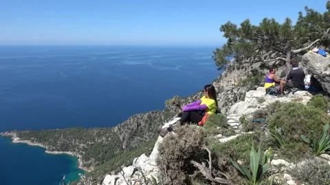 Hikers sitting on a mountain cliff edge overlooking the Mediterranean Sea Stock Footage 333464669