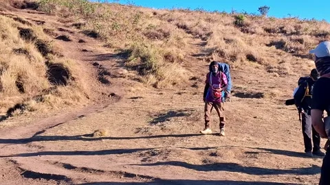 Hikers walking uphill on a dirt path under the bright morning sun Stock Footage 342090740