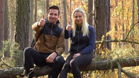 A hiking couple sits on a broken tree in a forest and show a thumb up to the Stock-Footage 109435788