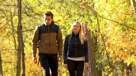 A hiking couple walks down a path through a forest on a sunny day - front view 스톡 동영상 109434059