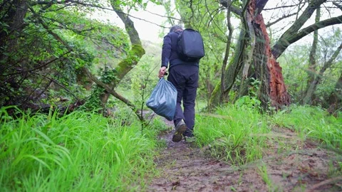 Hiking man with a garbage bag walking through the forest after picking up the Vidéo 309028688
