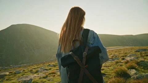 Hiking on a mountain path during sunset with a woman carrying a backpack looking Stock Footage 345631705