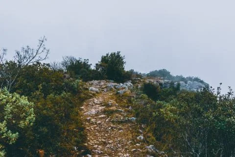 A hiking path on top of a mountain range under a cloud on a foggy morning in  Stock Photos