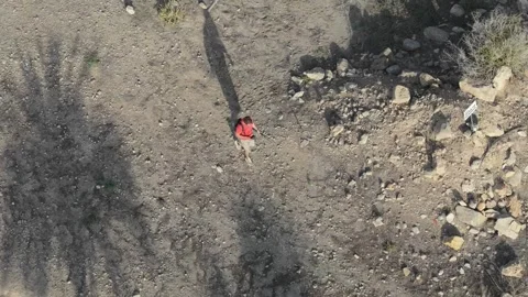 Hiking up a rocky mountain path, a man in a red shirt and shorts, equipped .. Stock Footage 283722695