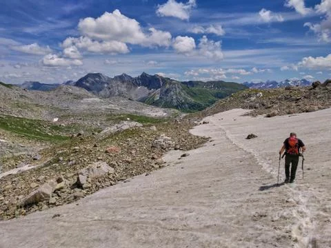 Hiking through snowfields in the mountains during summer. Hiker walking throu Stock Photos