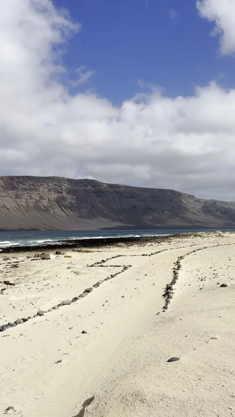 Hiking by Volcanic Shore with Risco de Famara view of La Graciosa Stock Footage 320007272
