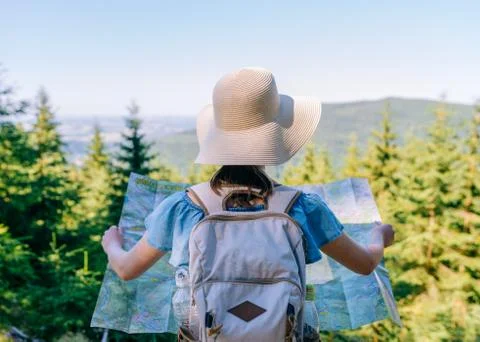Hiking woman traveler at the crossroads with backpack checks map to find dire Stock Photos