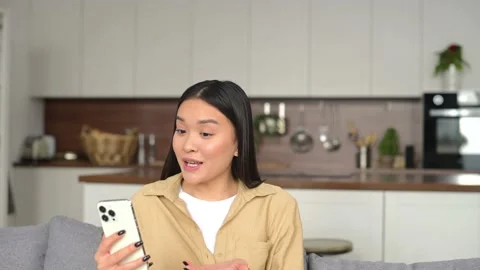 Hilarious asian woman using smartphone for video connection while sitting at the Stock Footage
