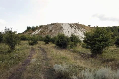 A hill with a light-colored slope rises in the background under a cloudy sky Stock Photos