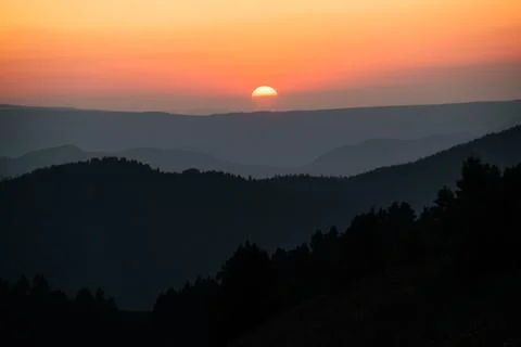 Hills, forest and the sun setting behind the mountains Stock Photos