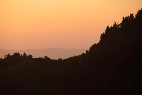 Hills, forest and the sun setting behind the mountains Stock Photos
