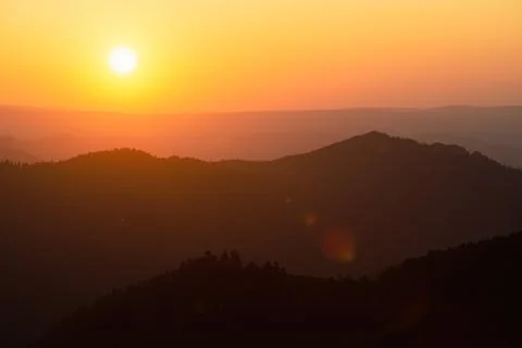 Hills, forest and the sun setting behind the mountains Stock Photos