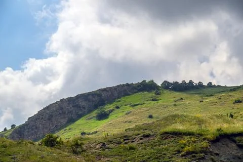Hillside covered in green grass under partly cloudy sky Stock Photos